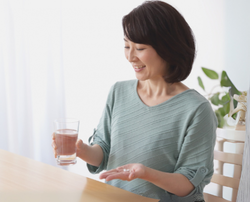 Asian woman holding glass of water in one hand and vitamins in another